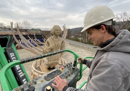 Man operating machinery in front of Wake sculpture
